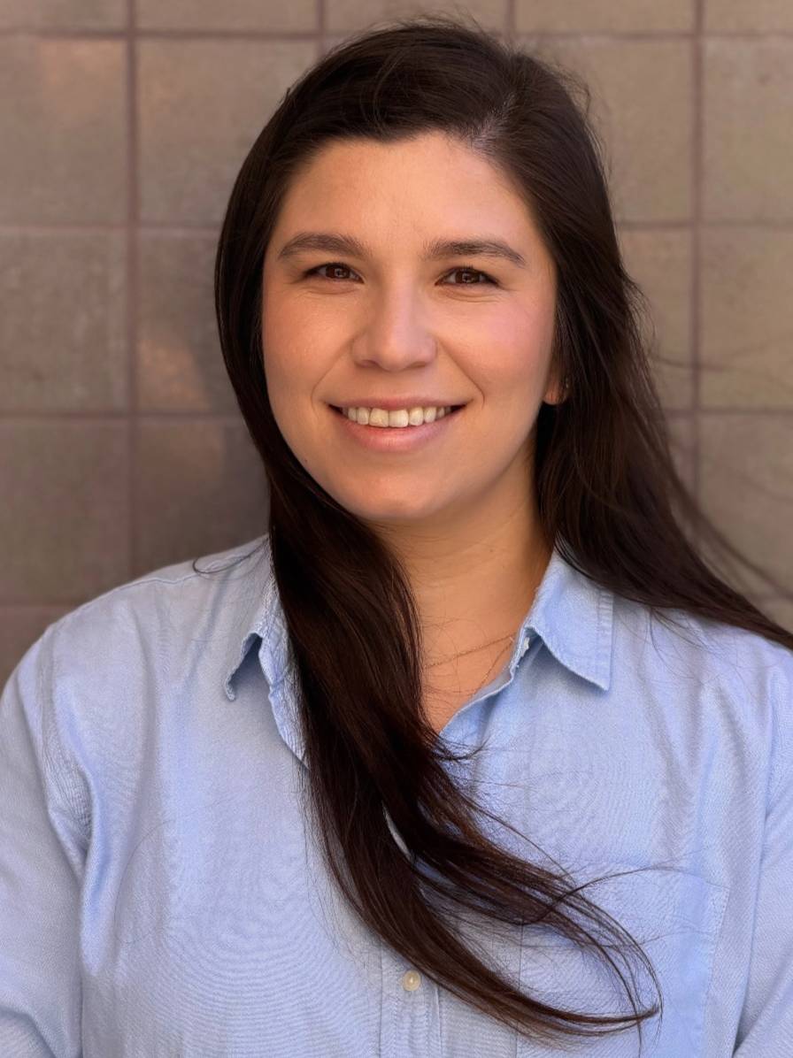 A smiling woman with long dark hair wearing a light blue button-down shirt.